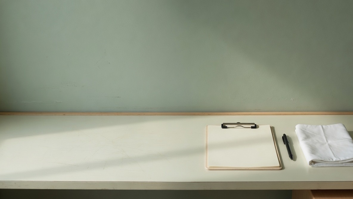 A blank clipboard, a pen and a folded cloth on a clinic bench.